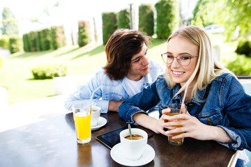 Young romantic couple spending time together - sitting in cafe's garden, drinking juice and having fun