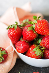Fresh ripe strawberry in a white bowl close-up against a background of napkin and table