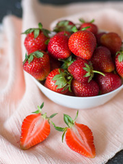 Fresh ripe strawberry in a white bowl close-up against a background of napkin and table