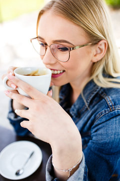 Young beautiful blond woman drinks coffee while sitting at cafe (outdoor)