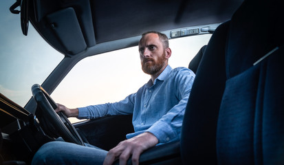 A bearded man in a shirt driving a car with a blue salon.