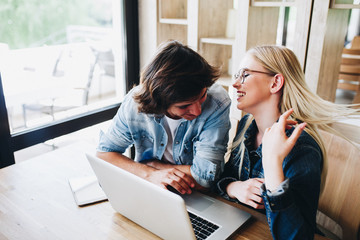 Young charming couple using laptop while sitting at cafe