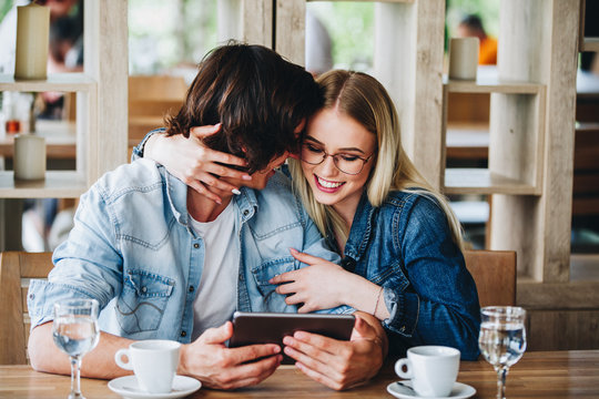 Young Charming Couple Using Tablet While Sitting Together And Drinking Coffee