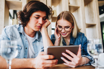 Young Charming Couple Using Tablet While Sitting Together And Drinking Coffee