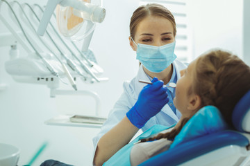Open mouth. Competent dentist using instrument while examining her visitor