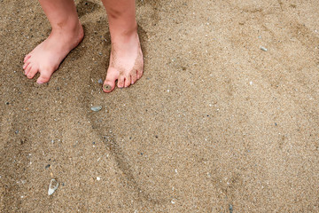 A little girl's / child's feet in the sand on a beach. Blank empty copy space for text.