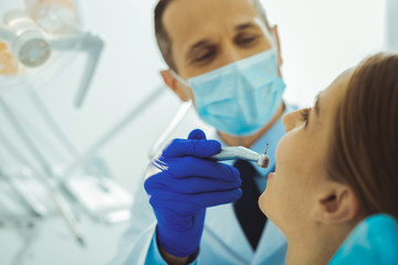 Do not be scared. Delighted medical worker using special equipment while filling a tooth