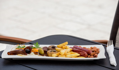 Traditional american breakfast, sausages, eggs, beans, french fries, and decorative vegetables, served on a plate, restaurant, service