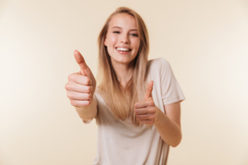 Image of attractive caucasian woman wearing casual clothing smiling and showing thumb up meaning good result or choice, isolated over beige background in studio