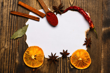 Spices, kitchen herbs lay around white paper. Culinary recipe concept. Piece of paper on wooden background. Cinnamon, dried orange and pepper, star anise lay around blank paper for recipe, copy space