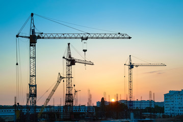 Industrial landscape with silhouettes of constraction cranes on sunset background