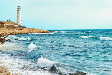 Old lighthouse on the sea coast. Storm, waves and blue sky