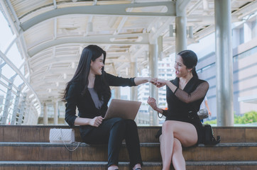 teamwork concept of business woman sitting on concrete stair at outdoor modern city  take fist bump for relationship and success together.