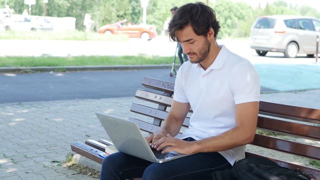 handsome young man student working with laptop computer outdoor in a street during summer