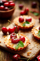 Tarts with fresh cherries and vanilla custard and caramel, delicious dessert on a wooden table, close up