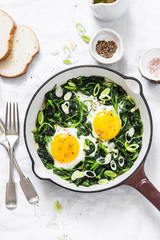 Green shakshuka. Fried eggs with fresh spinach, ramson, leek in a cast iron skillet on a white background, top view