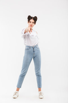 Full length portrait of serious strict girl having double buns hairstyle pointing finger at camera with blame, isolated over white background in studio