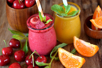Yellow and red smoothies in glass jars surrounded by mandarins and cherries