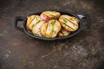 Grilled Potatoes with Chives in a Cast Iron Bowl on a Dark Background