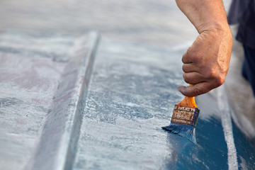 Man painting boat.Closeup view of hand holding a paintbrush with blue color.