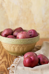 Fresh, Raw, Red Potatoes in a Vintage Bowl on a Wood Table with Yellow Plaster Wall in the Background