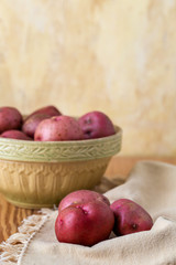 Fresh, Raw, Red Potatoes in a Vintage Bowl on a Wood Table with Yellow Plaster Wall in the Background