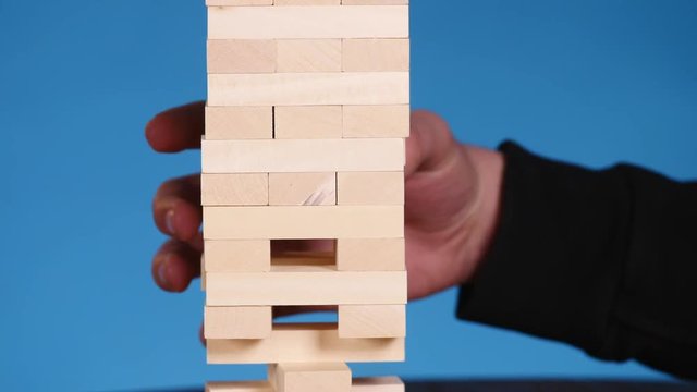 hands of Young man plays jenga on blue background, close-up. A man builds a tower of blocks while playing jenga