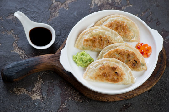 White plate with fried potstickers on a rustic wooden serving board, studio shot over brown stone surface