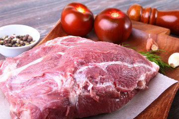 Raw pork steaks on wooden board with herbs, spices, tomatoes and pepper grinder ready for cooking. Selective focus