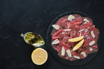 Carpaccio marbled beef served on a stone slate, above view on a black stone background, horizontal shot with space