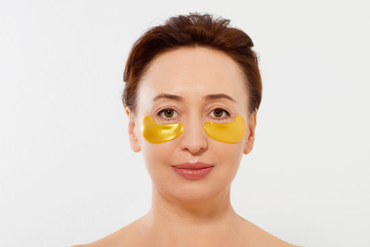 Macro female face. Beauty portrait of middle age woman with wrinkles and a gold patch under eye isolated on white background. Collagen mask and spa concept. Copy space. Summer skin care