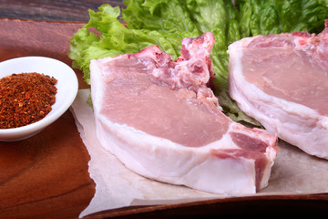 Raw pork steak with spices Leaves lettuce on wooden cutting board. Ready for cooking.