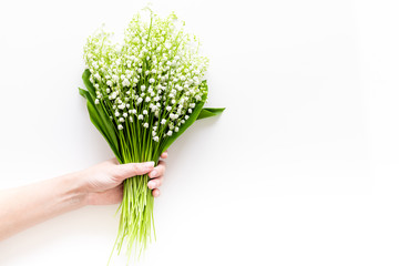 Give a bouquet of delicate lily of the valley flowers. Hand hold bunch of flowers on white background top view copy space