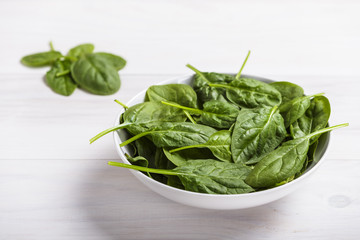 Ceramic bowl with fresh spinach on white wooden table background