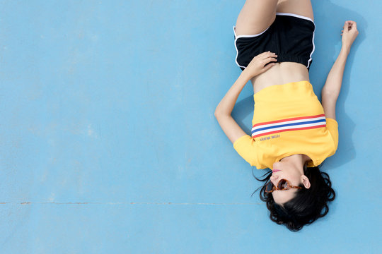 Woman in sportswear and sunglasses lying on blue
