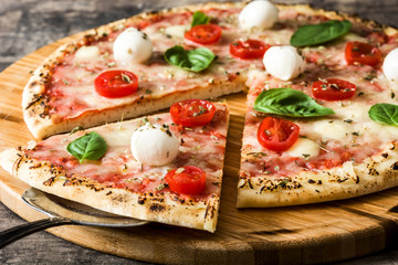 Italian pizza slice with tomatoes, cheese and basil on wooden table. Copyspace