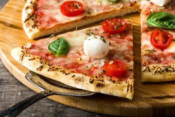 Italian pizza slice with tomatoes, cheese and basil on wooden table. Copyspace