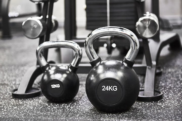 Naklejka na ściany i meble Two steel black kettlebells on the gray floor in the modern gym, monochrome color tone. Sports equipment for weight training.