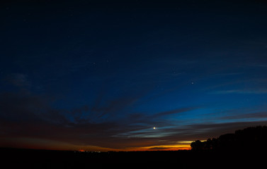 Venus in the night sky with stars. A bright sunset with clouds. Cosmic space above the earth's surface. Long exposure.