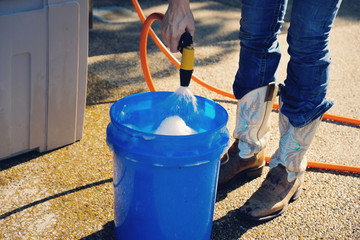 Woman spraying hose into blue bucket during summer to wash.