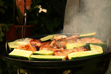 Ein Mann grillt im Garten am Kugelgrill Fleisch und Gemüse