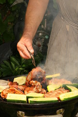 Ein Mann grillt im Garten am Kugelgrill Fleisch und Gemüse