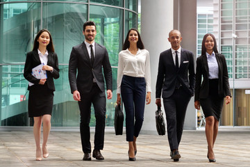 A group of business people of different ethnicities dressed in suits and ties walks proudly after leaving the offices. Concept of: team, success, connection and internationality.