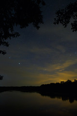 Fototapeta premium Space with stars in the night sky. The landscape with the river and trees is photographed on a long exposure.