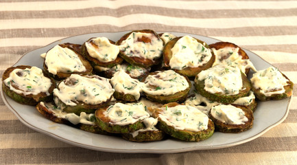 Appetizer from fried zucchini slices with mayonnaise and chopped dill.