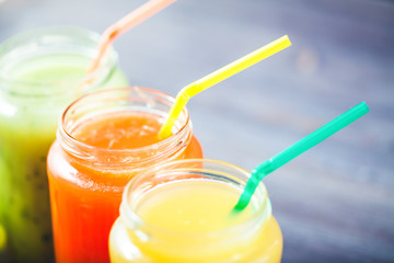 freshly squeezed fruit juice, smoothies yellow orange green blue banana lemon apple orange kiwi grape strawberry on a dark wooden background Close up
