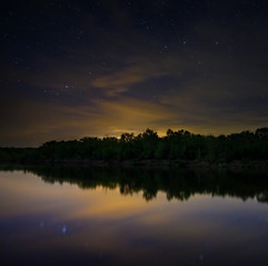 Obraz premium Space with stars in the night sky. The landscape with the river and trees is photographed on a long exposure.