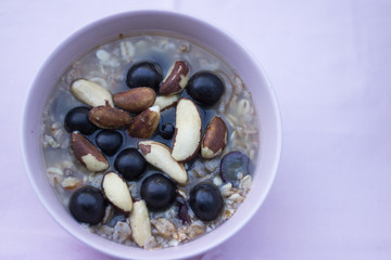 Muesli with water, with black grapes and Brazil nuts is on a pink background. Grapes is a known antioxidant. Fresh cereal breakfast. Top view. Concept: healthy food.