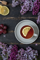 Tea Cup with lemon, grape and honey spoon on wooden background with fresh cut lilac flowers 