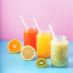 freshly squeezed fruit juice, smoothies yellow orange green lemon apple orange kiwi on bright blue and pink background Copy space.